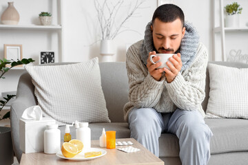 Ill young man drinking lemon tea on sofa at home
