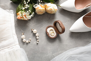 Wedding rings in wooden box, earrings, flowers and high heels on grey background. Top view
