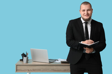 Office worker with notebook near table against blue background