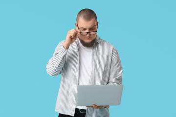 Surprised young man with laptop against blue background
