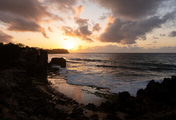 Sunrise reflected in the pacific ocean from a rocky cliff above the water in Hawaii