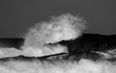 Monochrome photo of sea spray from a wave crashing on a rocky shore of Hawaii