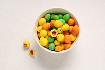 Bowl with colorful coated crunchy peanuts on light background