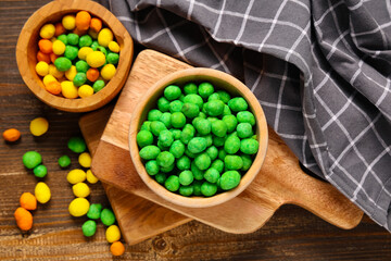 Bowls with colorful coated crunchy peanuts on wooden background
