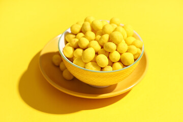 Bowl with cheese coated peanuts on yellow background