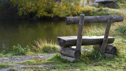 A roughly knocked together bench made of logs on the bank of a picturesque pond in the Elbrus region in autumn.