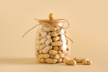 Jar with unpeeled peanuts on beige background