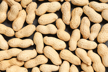 Many unpeeled peanuts on black background, closeup