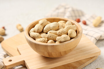 Wooden bowl with unpeeled peanuts on white background, closeup