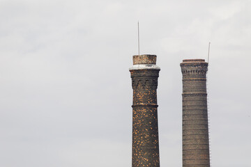 Two tall industrial chimneys made of dark brick, showing signs of aging and decay, standing against...