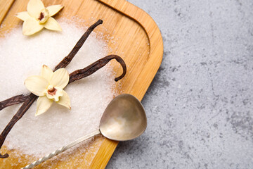 Wooden board of vanilla sugar with pods and flowers on grey background