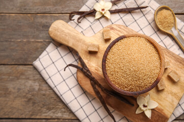 Bowl of vanilla sugar with pods and flowers on wooden background