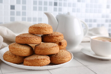 Plate with sweet cookies and cup of hot tea on white tile table
