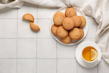 Plate with sweet cookies and cup of hot tea on white tile background