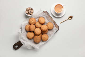 Wooden board with sweet cookies and cup of hot tea on white background