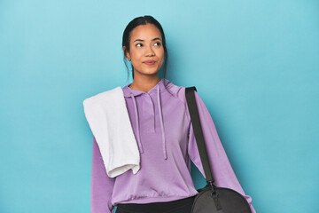 Filipina with gym gear on blue studio dreaming of achieving goals and purposes