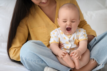 Young happy mother with her cute little yawning daughter sitting on bed at home