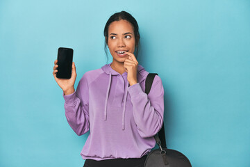 Filipina ready for gym with phone on blue relaxed thinking about something looking at a copy space.