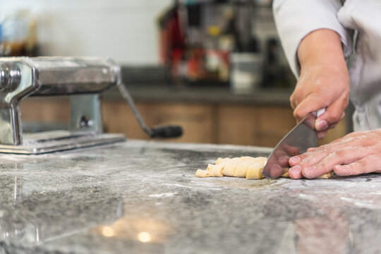 Chef cutting fresh pasta dough with knife in restaurant kitchen