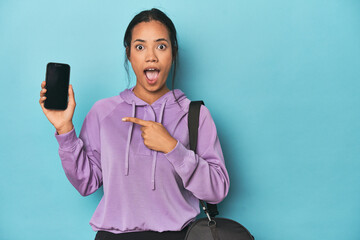 Filipina ready for gym with phone on blue pointing to the side
