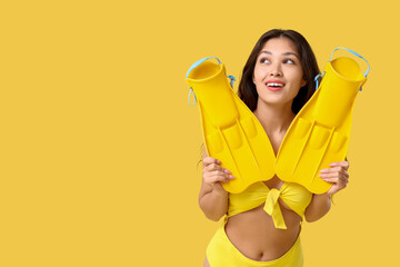 Beautiful young Asian woman in stylish yellow swimsuit with flippers on color background © Pixel-Shot