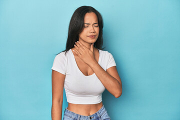 Filipina young woman on blue studio suffers pain in throat due a virus or infection.