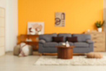 Blurred view of living room with grey sofa and table near yellow wall