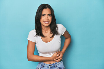 Filipina young woman on blue studio having a liver pain, stomach ache.