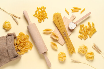 Composition with different types of raw pasta and rolling pin on beige background