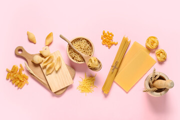 Composition with different types of raw tasty pasta, bowl and wooden cutting boards on pink background