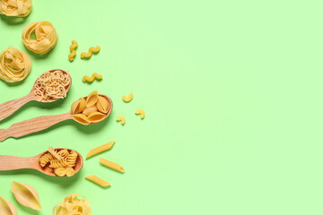 Composition with different types of raw tasty pasta and wooden spoons on green background