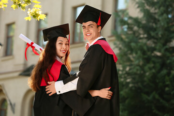 Couple of happy students with diplomas hugging on their graduation day, back view