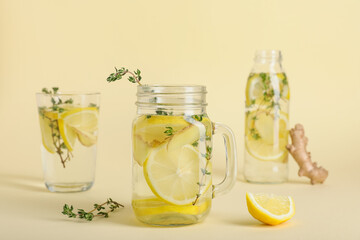 Mason jar and glass of fresh lemon infused water with ginger and thyme on yellow background