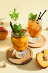 Glasses of tasty iced tea with mint and peaches on beige background