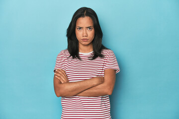 Filipina young woman on blue studio unhappy looking in camera with sarcastic expression.