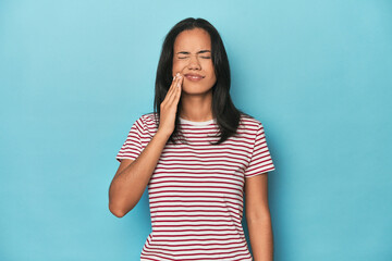 Filipina young woman on blue studio having a strong teeth pain, molar ache.
