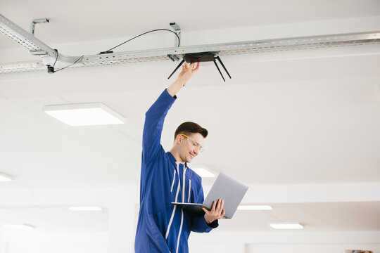 Technician installing wireless router on ceiling using laptop