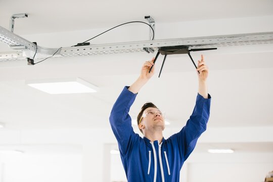 Technician installing wireless router on ceiling in office building