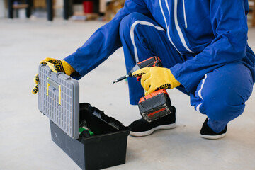 Construction worker taking electric screwdriver from toolbox wearing protective gloves
