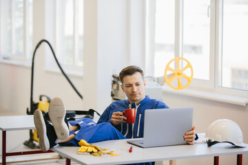 Worker relaxing with feet up on desk, drinking coffee and using laptop