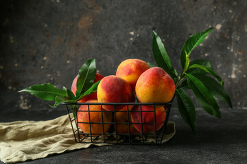 Basket with sweet ripe peaches and leaves on dark background