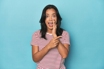 Filipina young woman on blue studio saying a gossip, pointing to side reporting something.