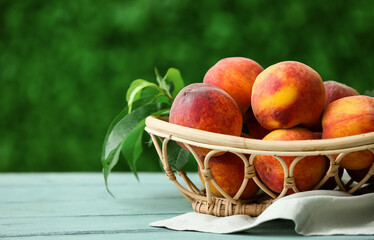 Wicker basket with sweet ripe peaches on blue wooden table outdoors