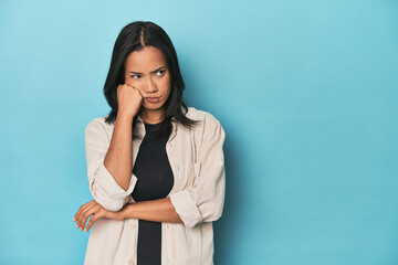 Filipina young woman on blue studio who feels sad and pensive, looking at copy space.