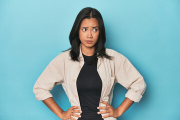 Filipina young woman on blue studio confused, feels doubtful and unsure.
