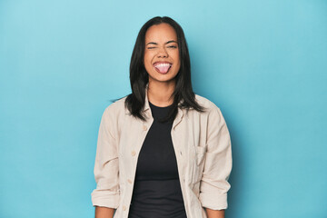 Filipina young woman on blue studio funny and friendly sticking out tongue.