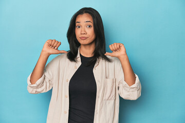 Filipina young woman on blue studio feels proud and self confident, example to follow.