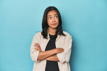 Filipina young woman on blue studio dreaming of achieving goals and purposes