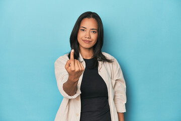 Filipina young woman on blue studio pointing with finger at you as if inviting come closer.