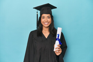 Celebrating Filipina graduate with diploma and cap on blue studio